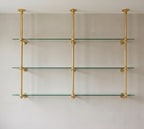 Front view of the two-bay brass bistro shelf with three ceiling-mounted posts and three clear glass shelves