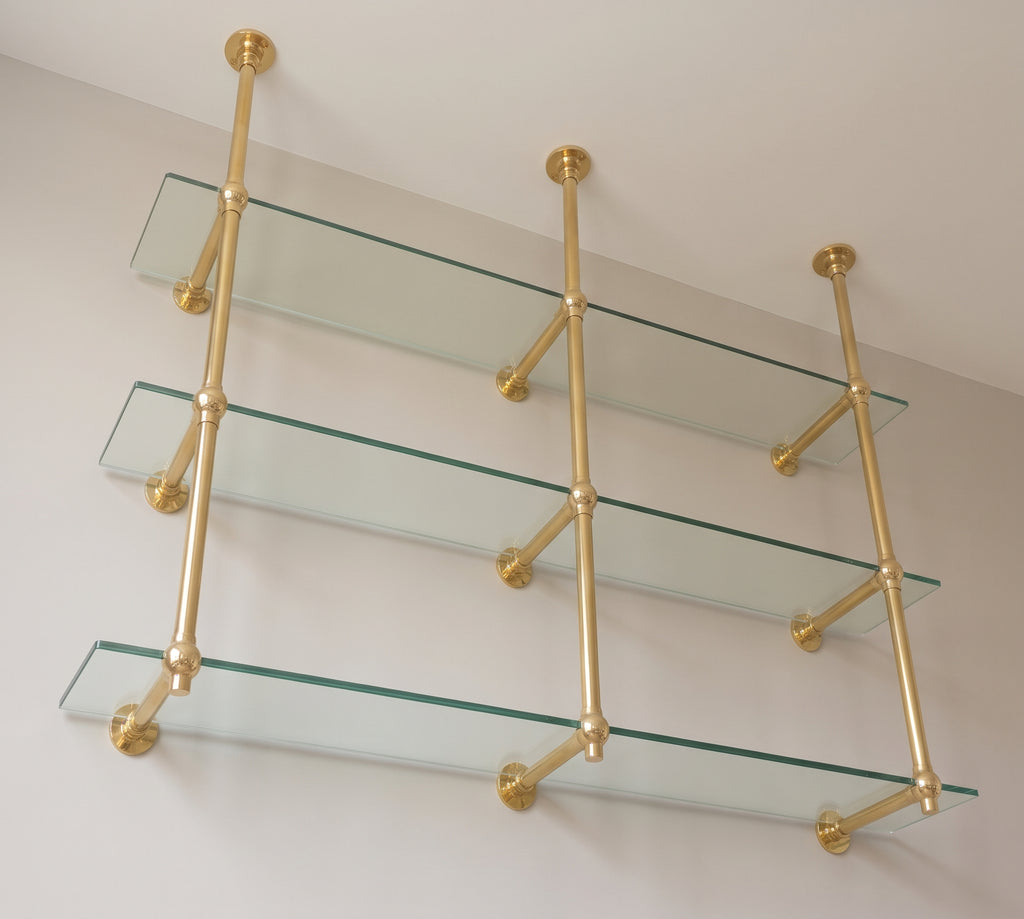 View from below of the brass wall support arms and ball joints under each glass shelf
