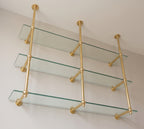 View from below of the brass wall support arms and ball joints under each glass shelf