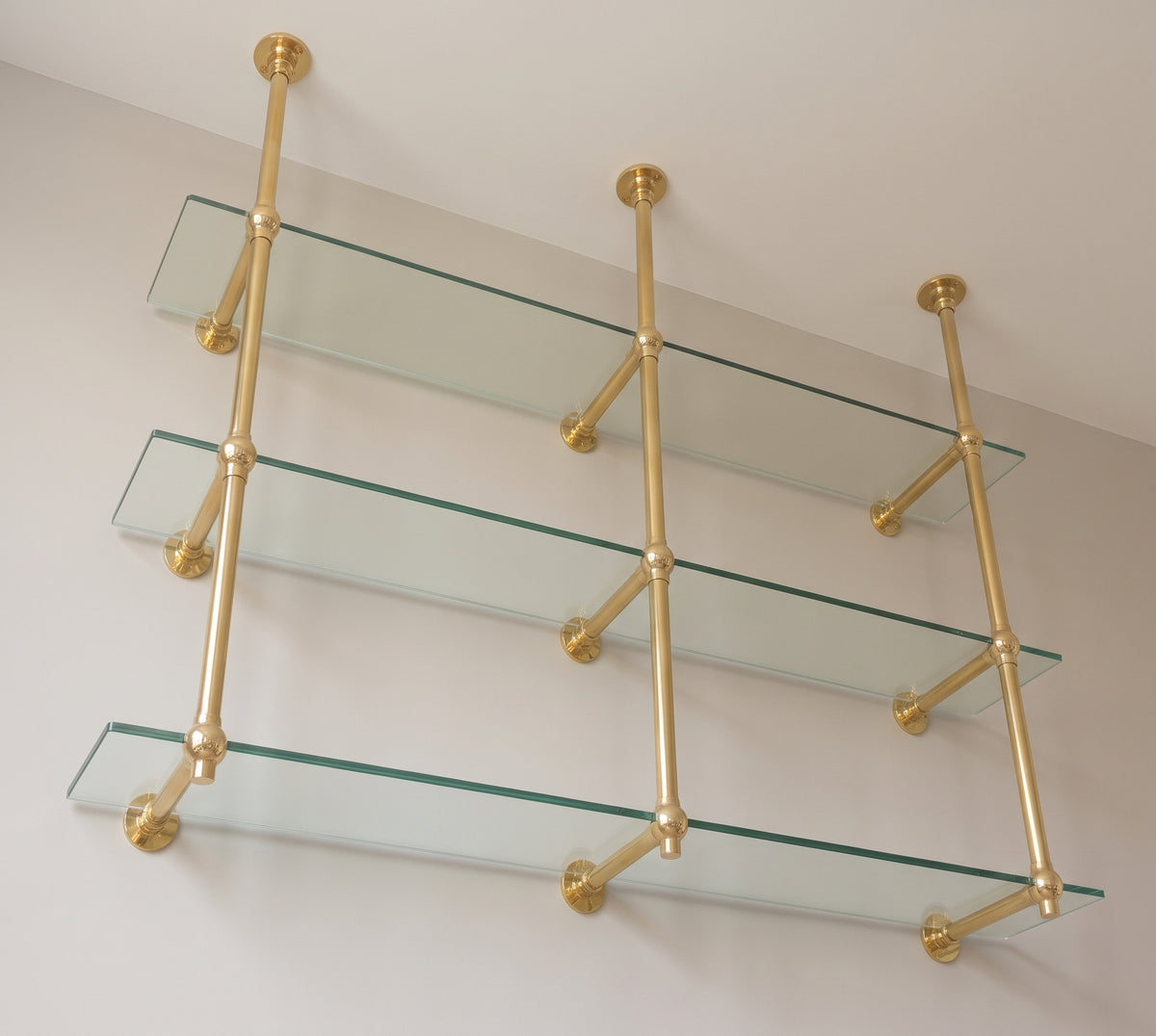View from below of the brass wall support arms and ball joints under each glass shelf