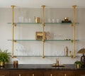 Two-bay brass and glass bistro shelf hung from the ceiling, styled with barware above a dark marble sideboard