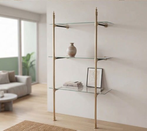 Two-post brass bistro shelf with three glass shelves standing against a living room wall